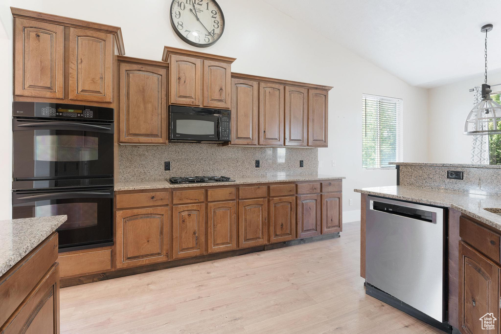 Kitchen featuring black appliances, lofted ceiling, backsplash, light wood-style flooring, and light stone countertops