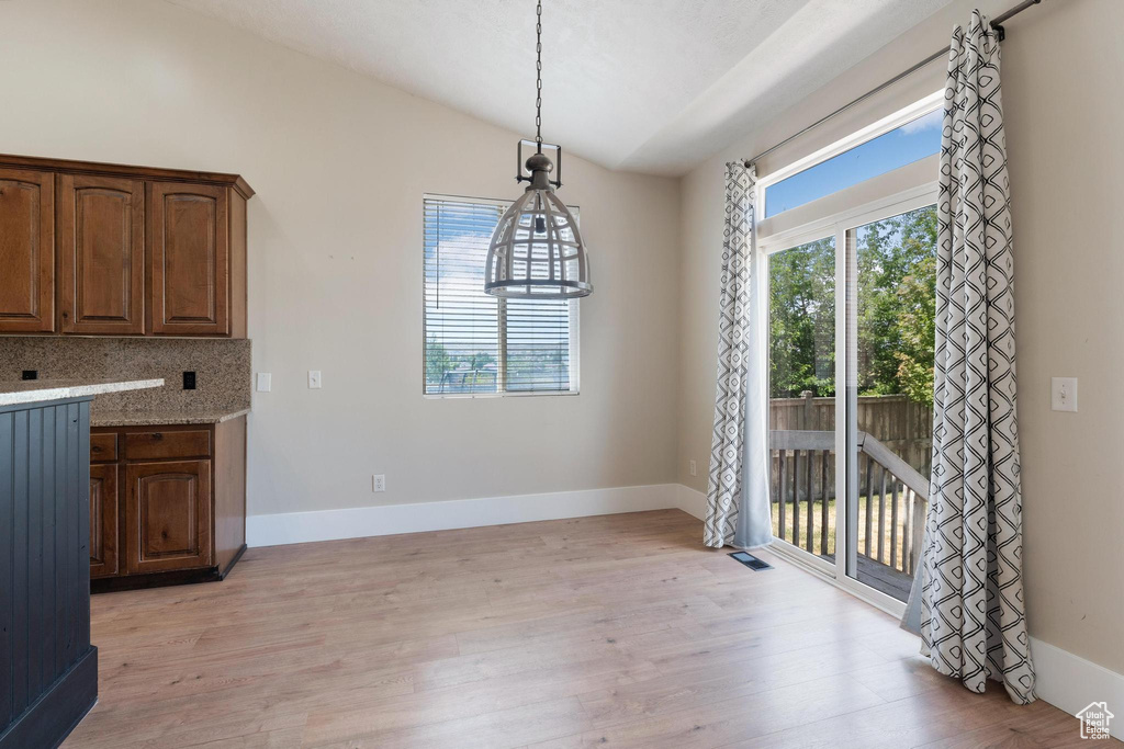 Unfurnished dining area featuring vaulted ceiling and light wood-style flooring