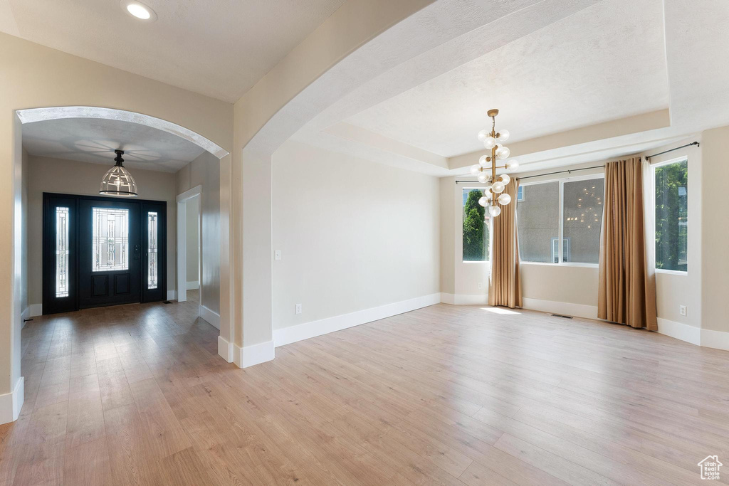 Entrance foyer with a chandelier, light wood-style floors, arched walkways, recessed lighting, and a raised ceiling