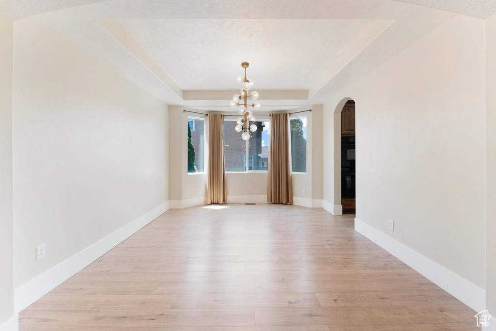 Unfurnished dining area with arched walkways, a raised ceiling, a chandelier, and light wood-type flooring