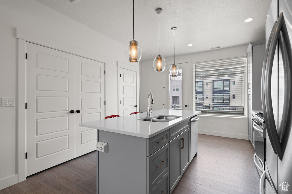 Kitchen featuring gray cabinetry, stainless steel appliances, light countertops, an island with sink, and wood finished floors