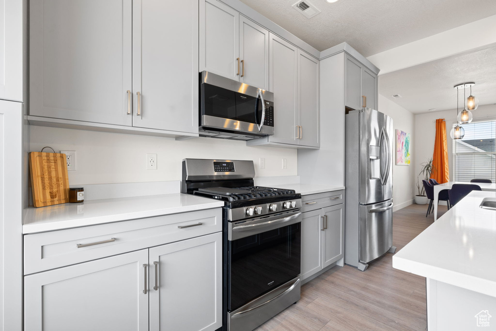 Kitchen featuring appliances with stainless steel finishes, light countertops, light wood-style floors, gray cabinets, and hanging light fixtures