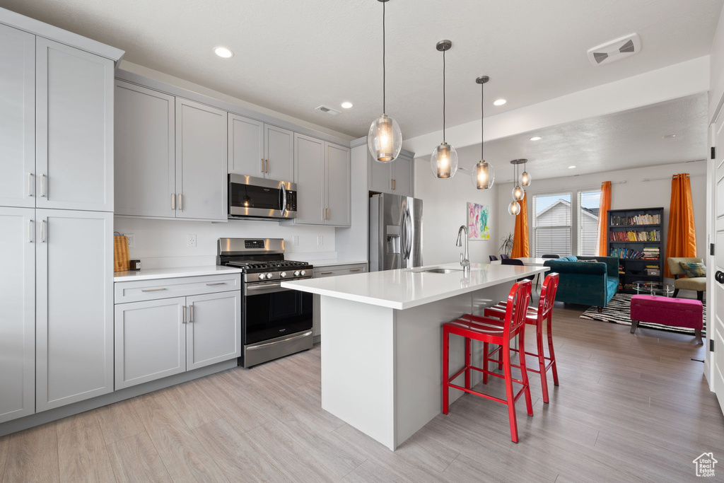 Kitchen featuring stainless steel appliances, light countertops, light wood finished floors, a breakfast bar, and recessed lighting