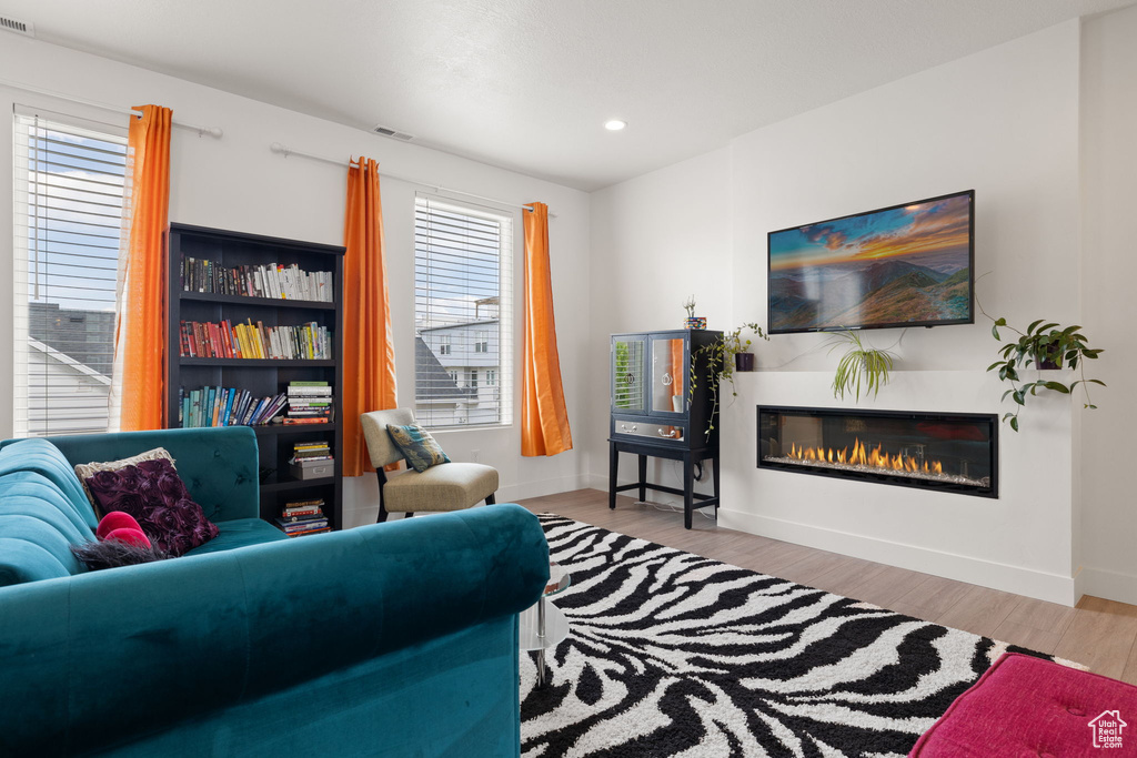 Living room featuring wood finished floors, a glass covered fireplace, and recessed lighting