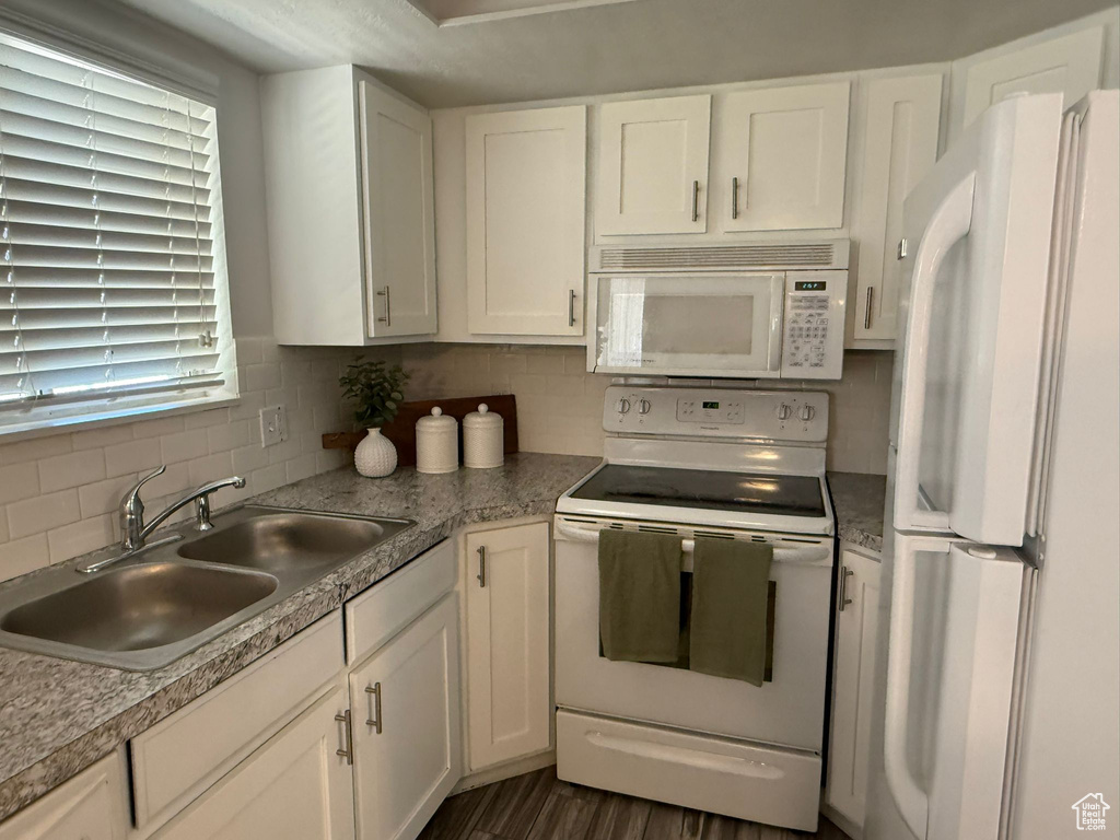 Kitchen with white appliances, a sink, decorative backsplash, white cabinetry, and light countertops