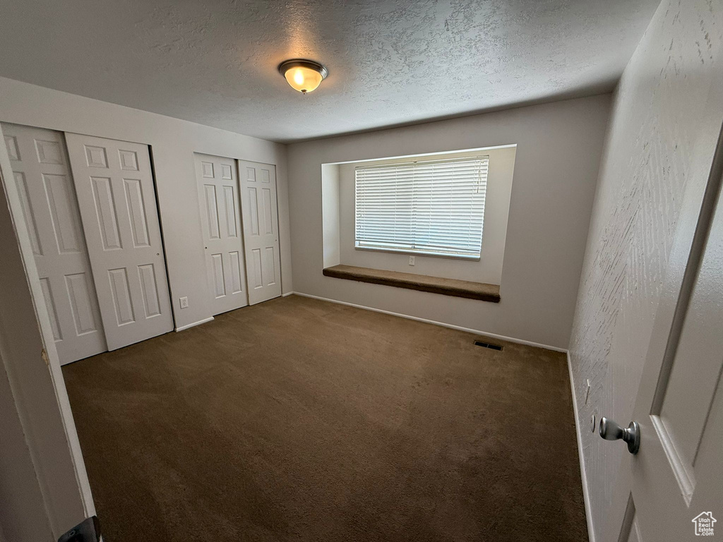 Unfurnished bedroom featuring multiple closets, carpet flooring, a textured ceiling, and baseboards