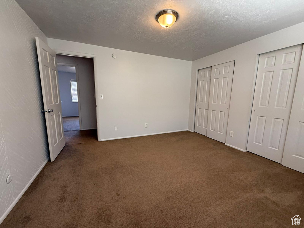 Unfurnished bedroom featuring carpet flooring, baseboards, two closets, and a textured ceiling