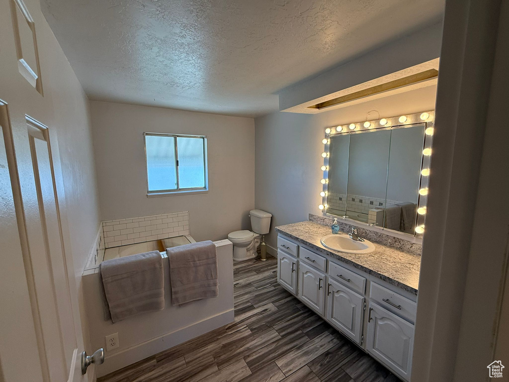 Bathroom featuring toilet, a textured ceiling, vanity, baseboards, and wood finished floors