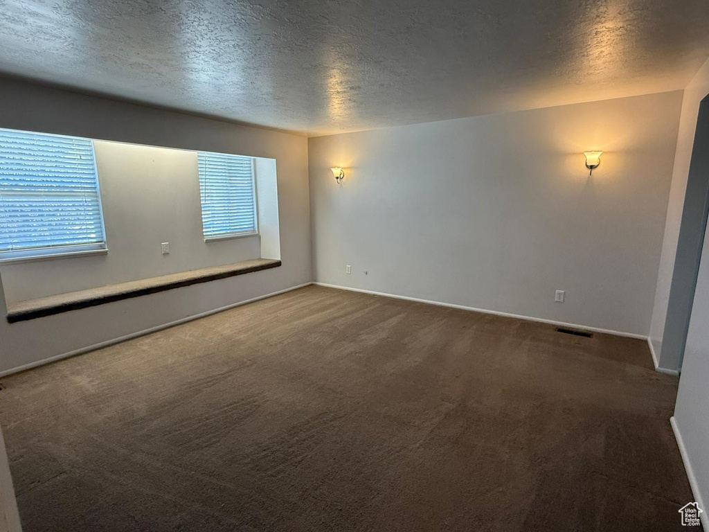 Carpeted empty room with a textured ceiling and baseboards