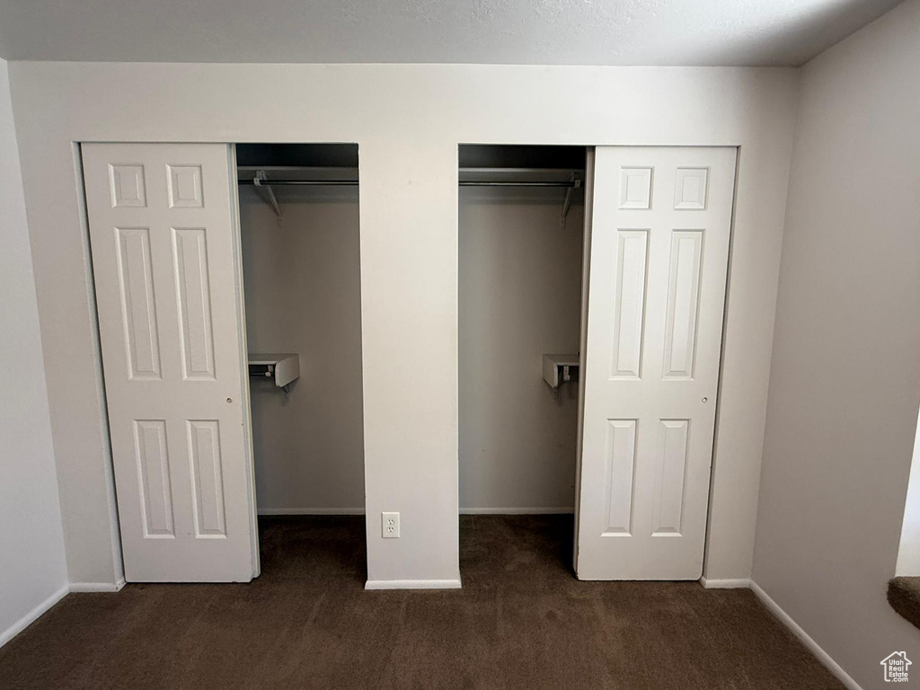 Unfurnished bedroom with dark colored carpet, two closets, and baseboards