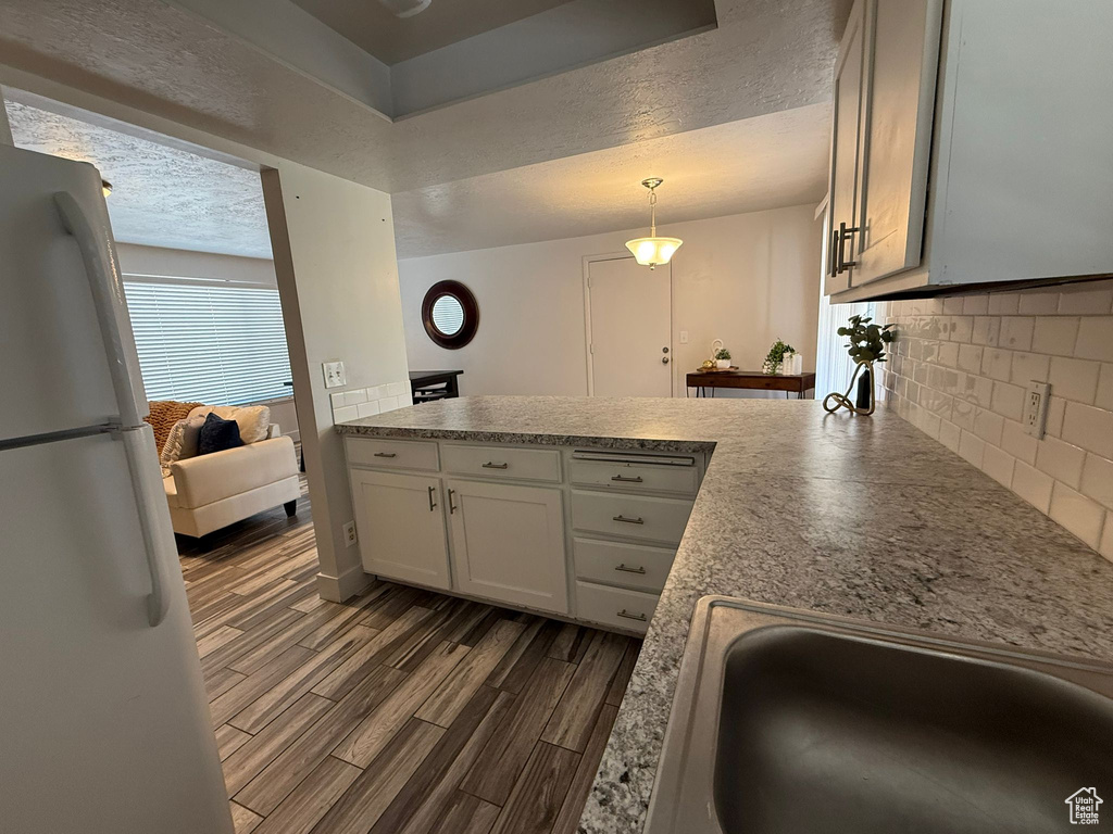 Kitchen with freestanding refrigerator, a peninsula, dark wood-type flooring, decorative backsplash, and a textured ceiling