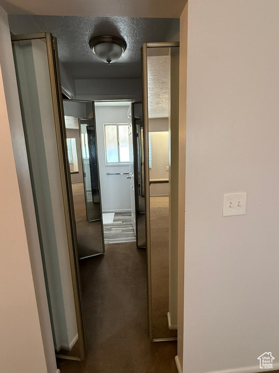 Hallway featuring dark colored carpet, baseboards, and a textured ceiling