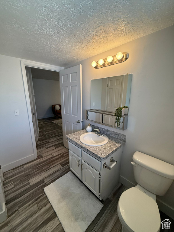 Bathroom featuring vanity, wood finished floors, toilet, a textured ceiling, and baseboards