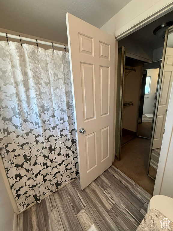 Full bath with curtained shower, toilet, and wood finished floors
