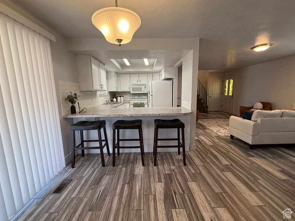 Kitchen featuring white appliances, dark wood finished floors, a sink, light countertops, and a breakfast bar area