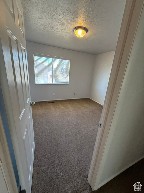 Carpeted empty room with a textured ceiling and baseboards
