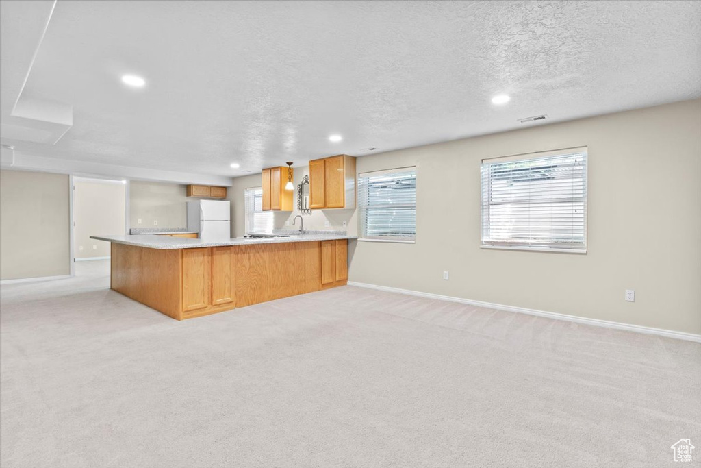 Kitchen featuring freestanding refrigerator, a peninsula, recessed lighting, light countertops, and light carpet