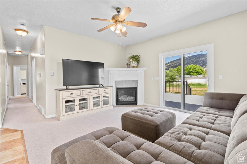Living area featuring light carpet, ceiling fan, and a fireplace with flush hearth