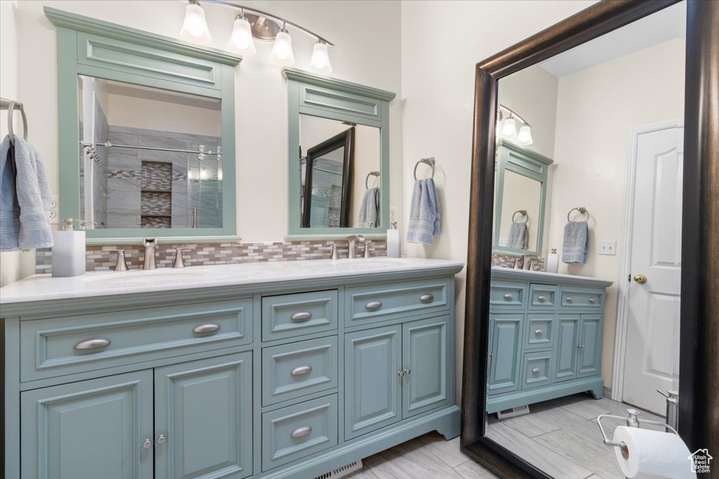 Full bath with double vanity, a shower stall, and tasteful backsplash