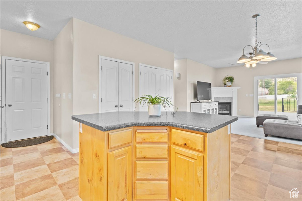 Kitchen featuring dark countertops, a textured ceiling, a chandelier, a glass covered fireplace, and hanging light fixtures