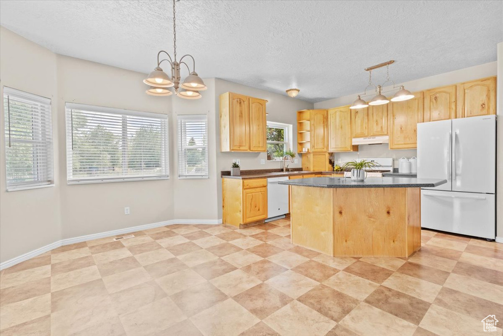 Kitchen with white appliances, light brown cabinets, dark countertops, a kitchen island, and a textured ceiling