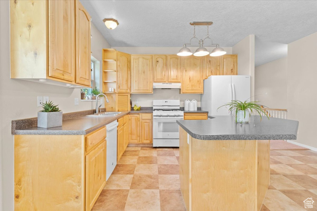 Kitchen featuring white appliances, light brown cabinets, dark countertops, under cabinet range hood, and a center island