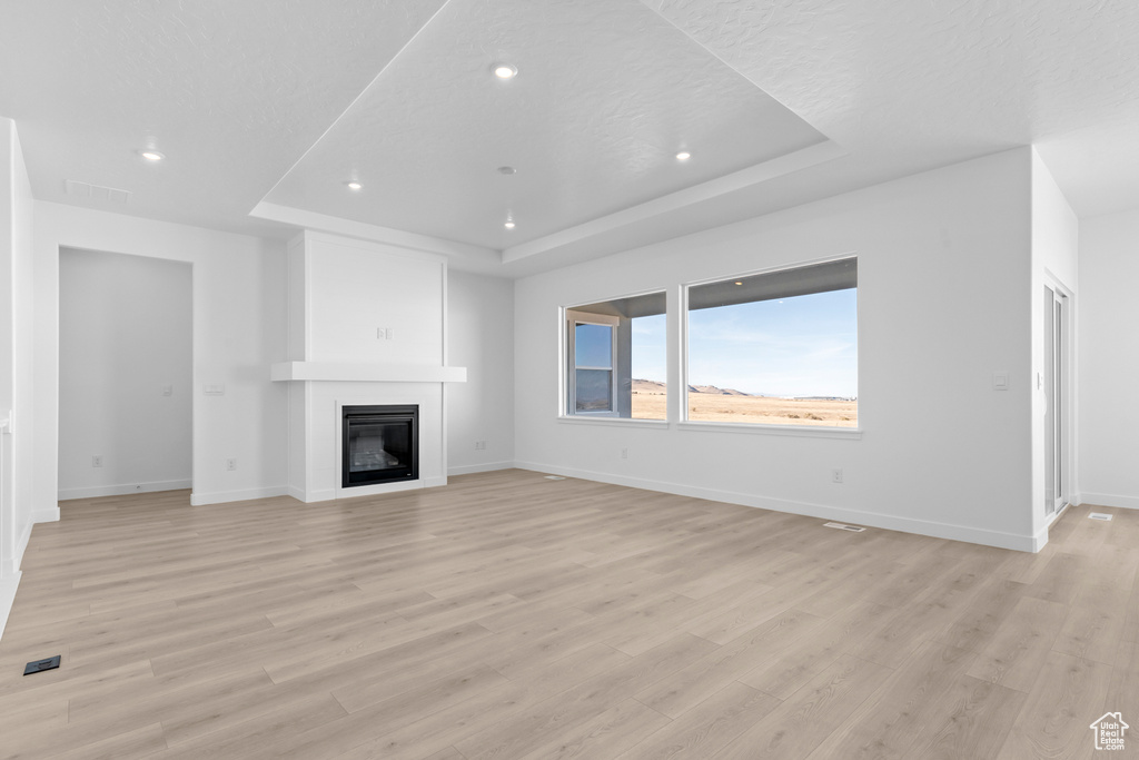 Unfurnished living room featuring a tray ceiling, light wood finished floors, recessed lighting, and a glass covered fireplace