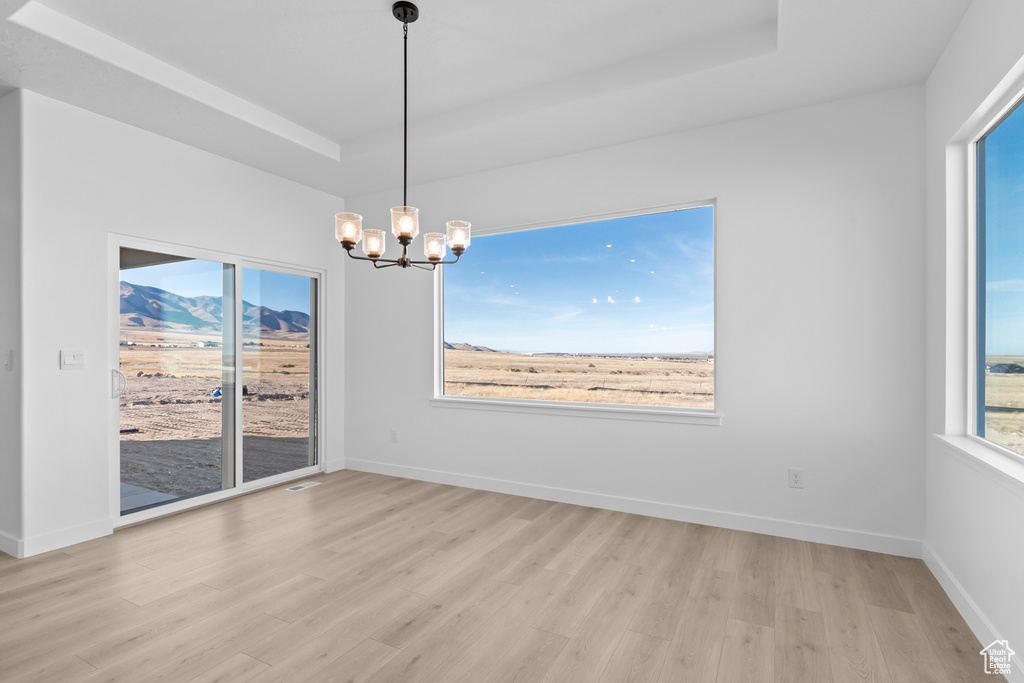 Empty room with light wood-type flooring, a chandelier, a raised ceiling, and a mountain view