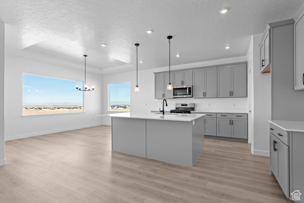Kitchen with appliances with stainless steel finishes, gray cabinetry, a tray ceiling, a chandelier, and a textured ceiling