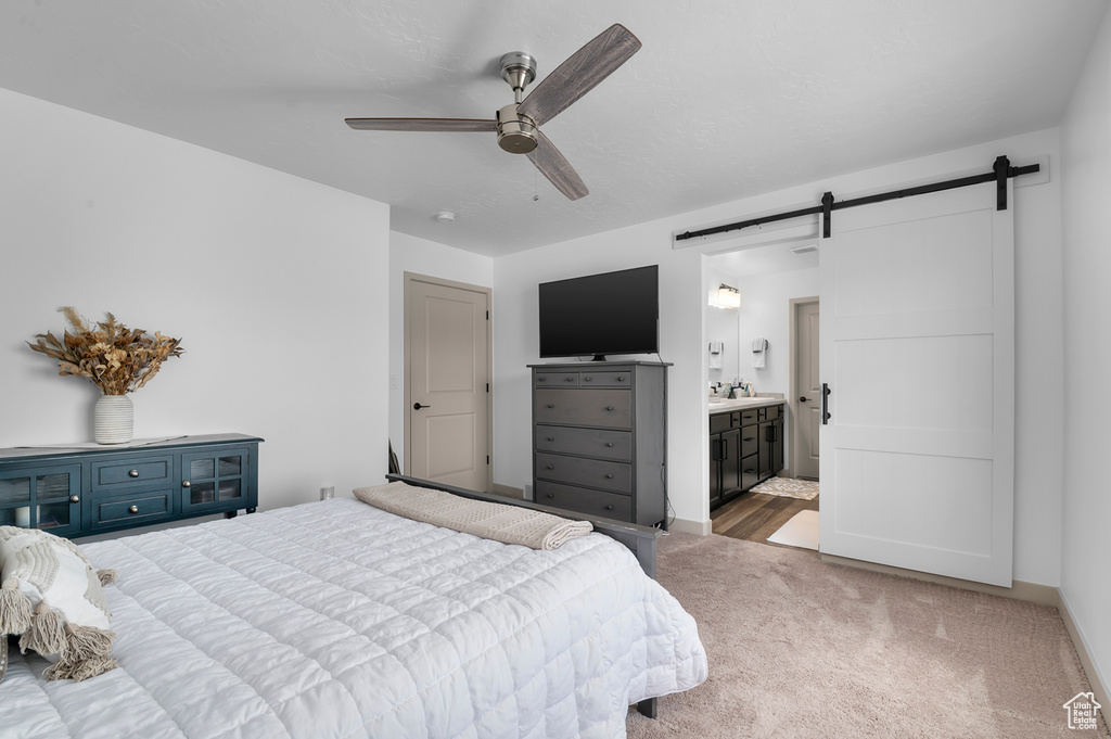 Carpeted bedroom featuring a barn door, ensuite bath, and a ceiling fan