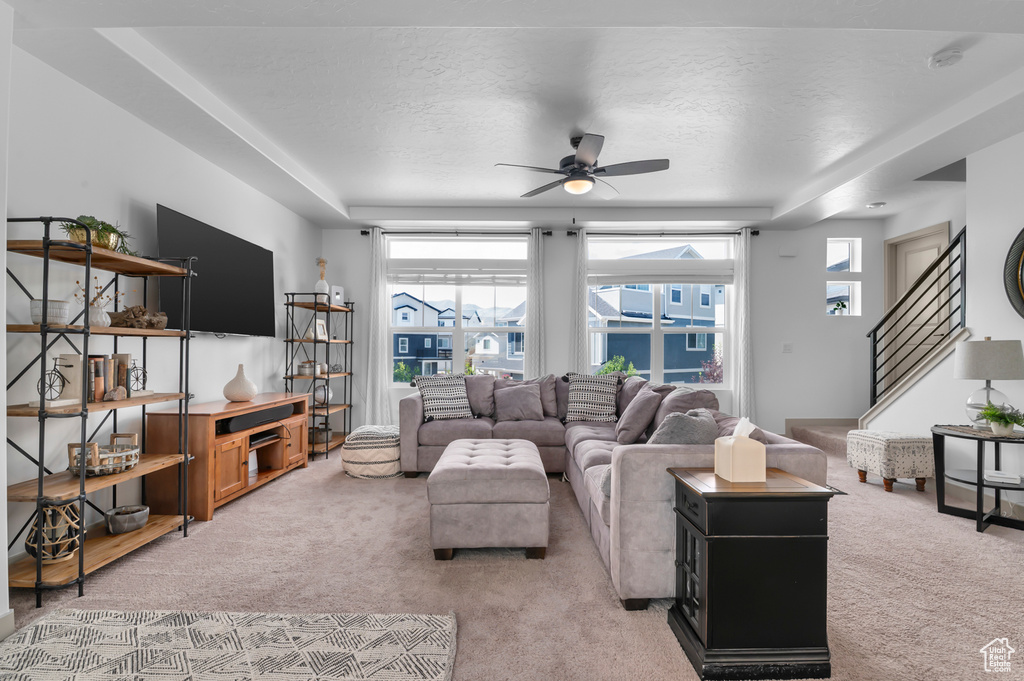 Living room with light colored carpet, healthy amount of natural light, a ceiling fan, a raised ceiling, and a textured ceiling