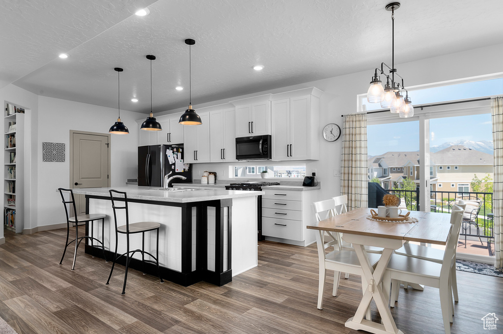 Kitchen with freestanding refrigerator, recessed lighting, wood finished floors, an island with sink, and light countertops