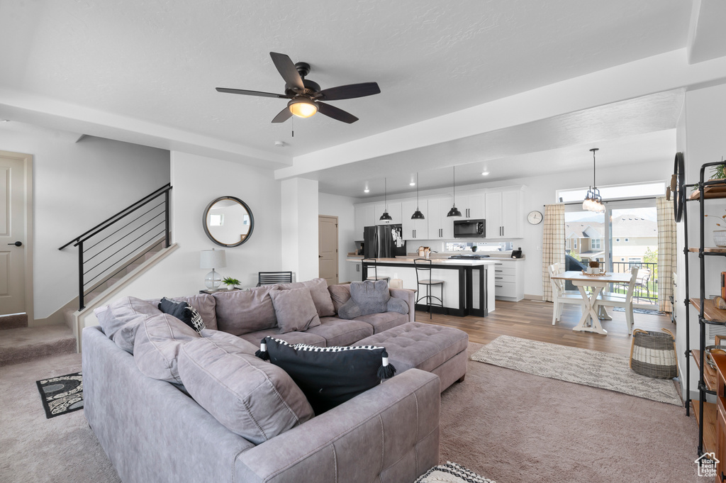 Living area with light colored carpet, a ceiling fan, and stairway