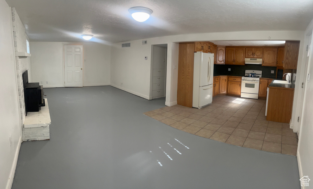 Kitchen with white appliances, ventilation hood, brown cabinets, open floor plan, and a brick fireplace