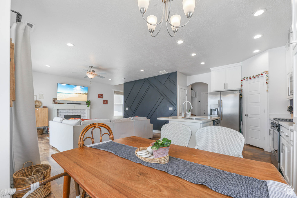 Dining space featuring a ceiling fan, arched walkways, recessed lighting, a chandelier, and a tiled fireplace