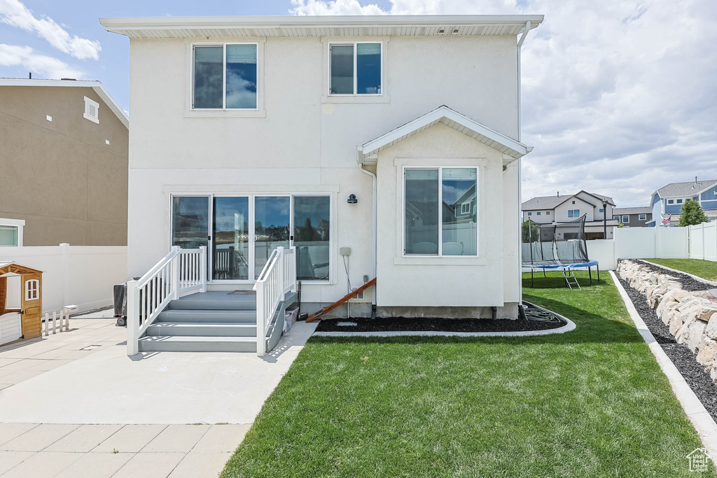 Rear view of property with stucco siding, a trampoline, and a patio area