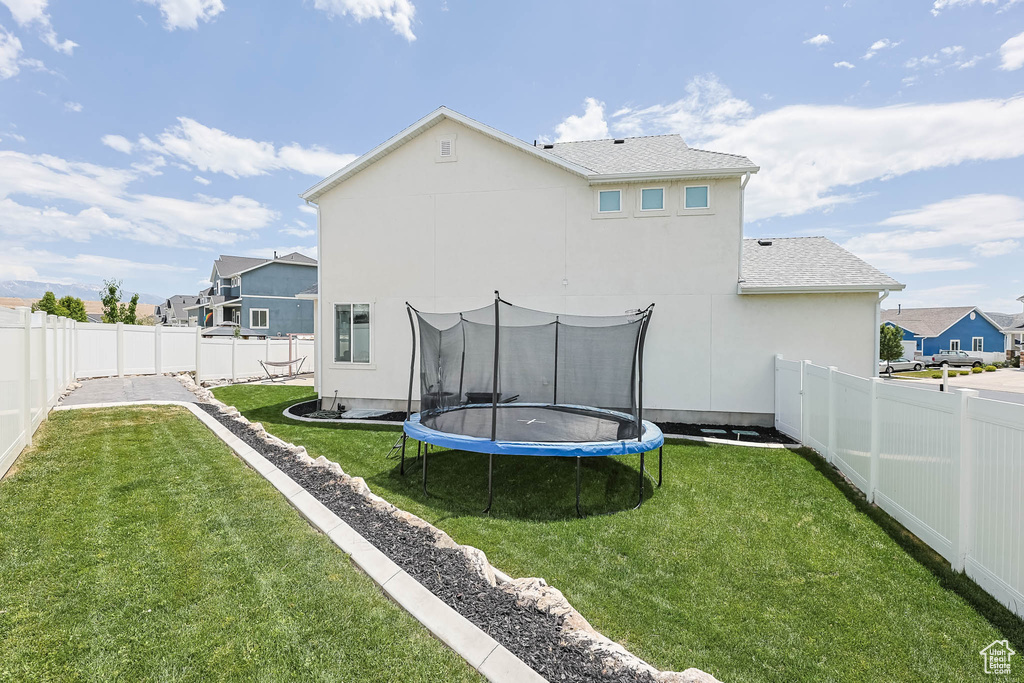 Back of property with a trampoline, stucco siding, a fenced backyard, and a residential view