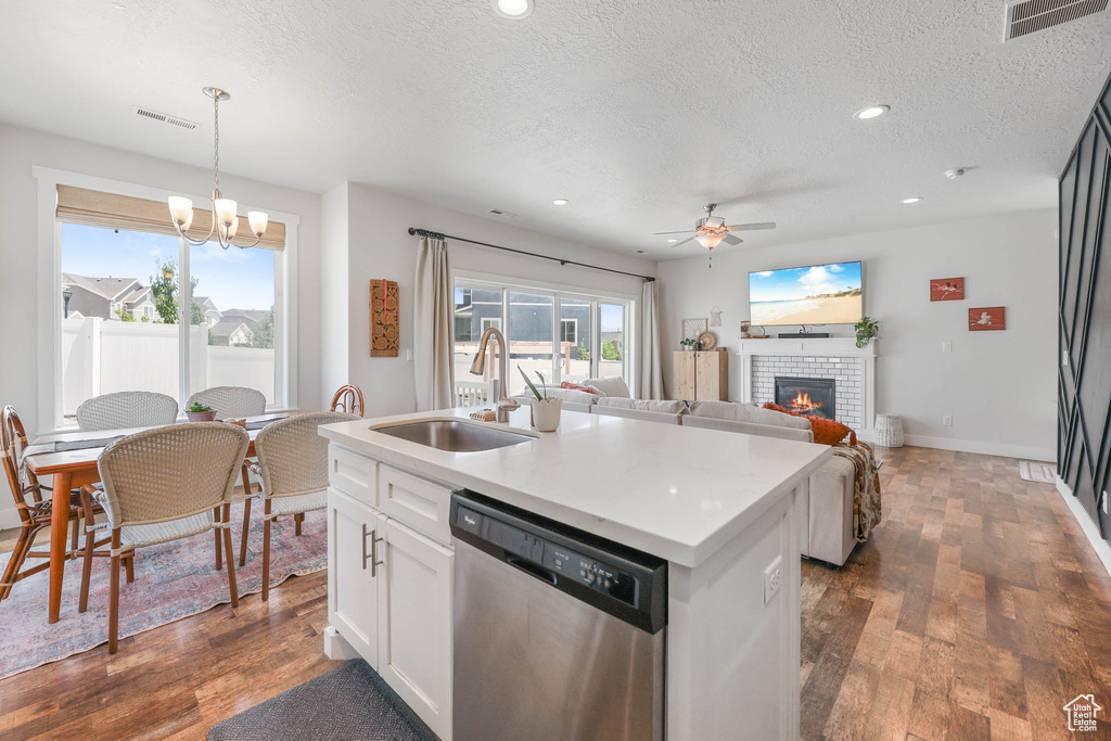 Kitchen with stainless steel dishwasher, a textured ceiling, ceiling fan, a fireplace, and white cabinetry