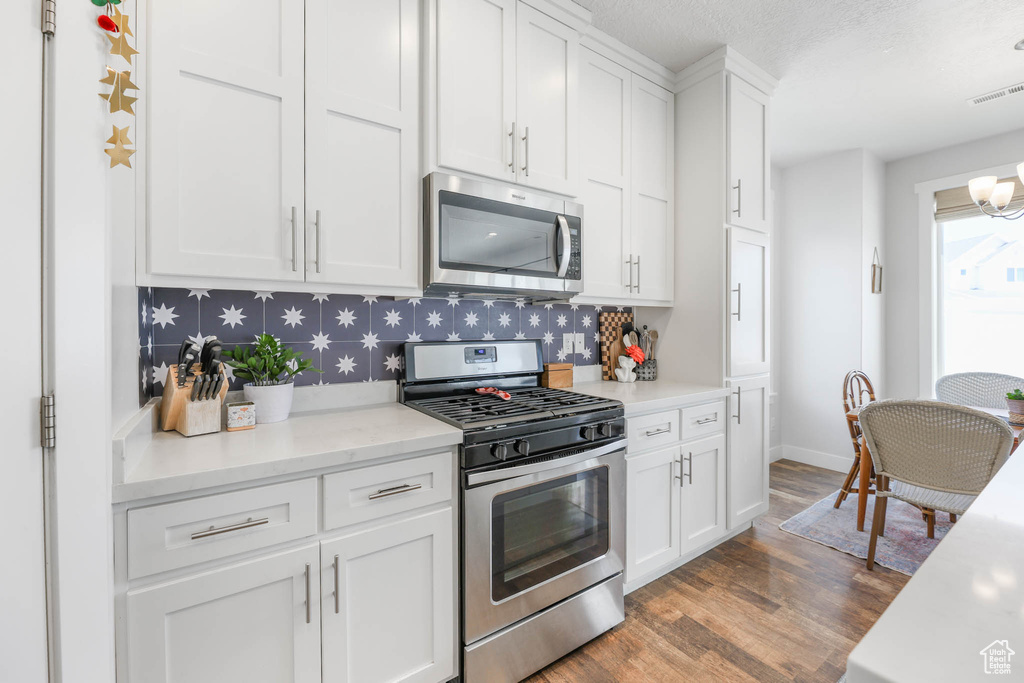 Kitchen with stainless steel appliances, wood finished floors, white cabinets, light countertops, and a chandelier
