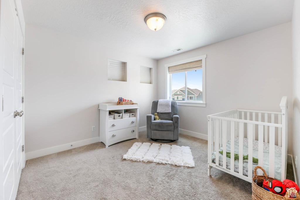 Bedroom with a nursery area, carpet flooring, and a textured ceiling