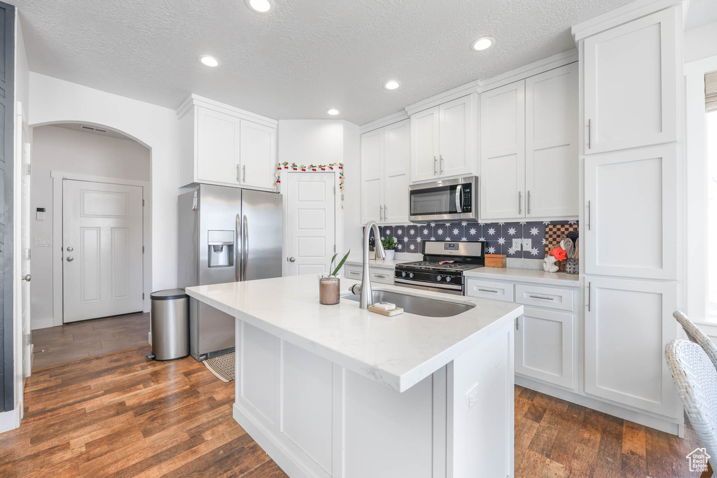 Kitchen featuring stainless steel appliances, arched walkways, white cabinets, light countertops, and backsplash