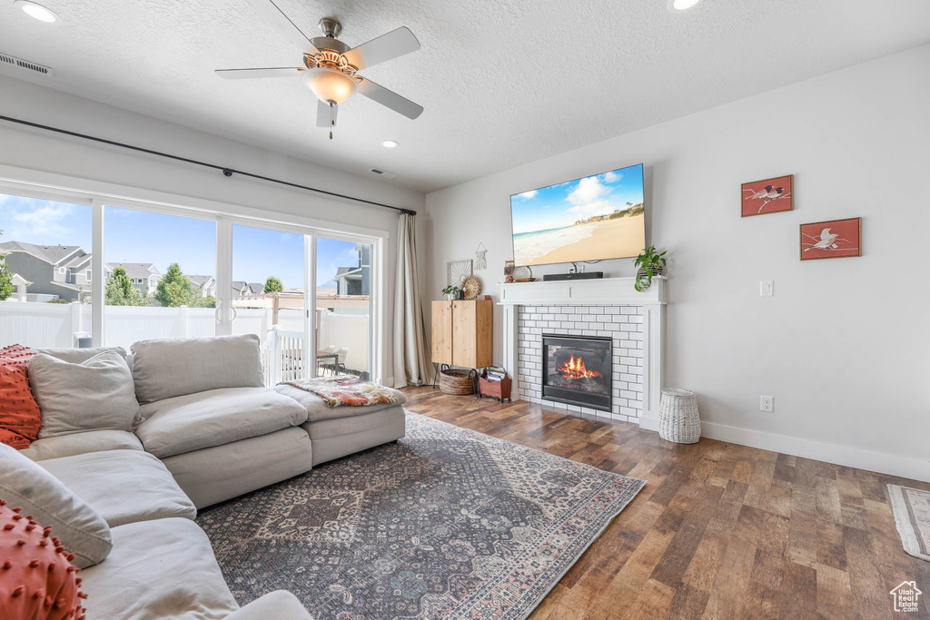 Living room featuring a brick fireplace, a ceiling fan, hardwood / wood-style flooring, recessed lighting, and a textured ceiling