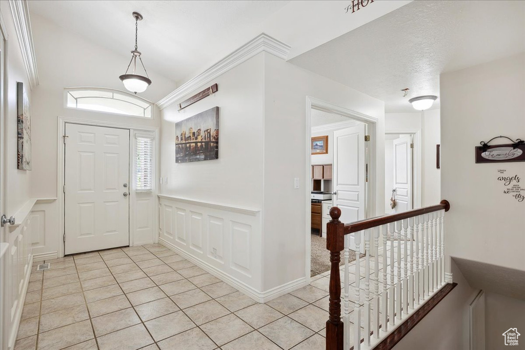 Foyer entrance with light tile patterned flooring, a decorative wall, wainscoting, and lofted ceiling