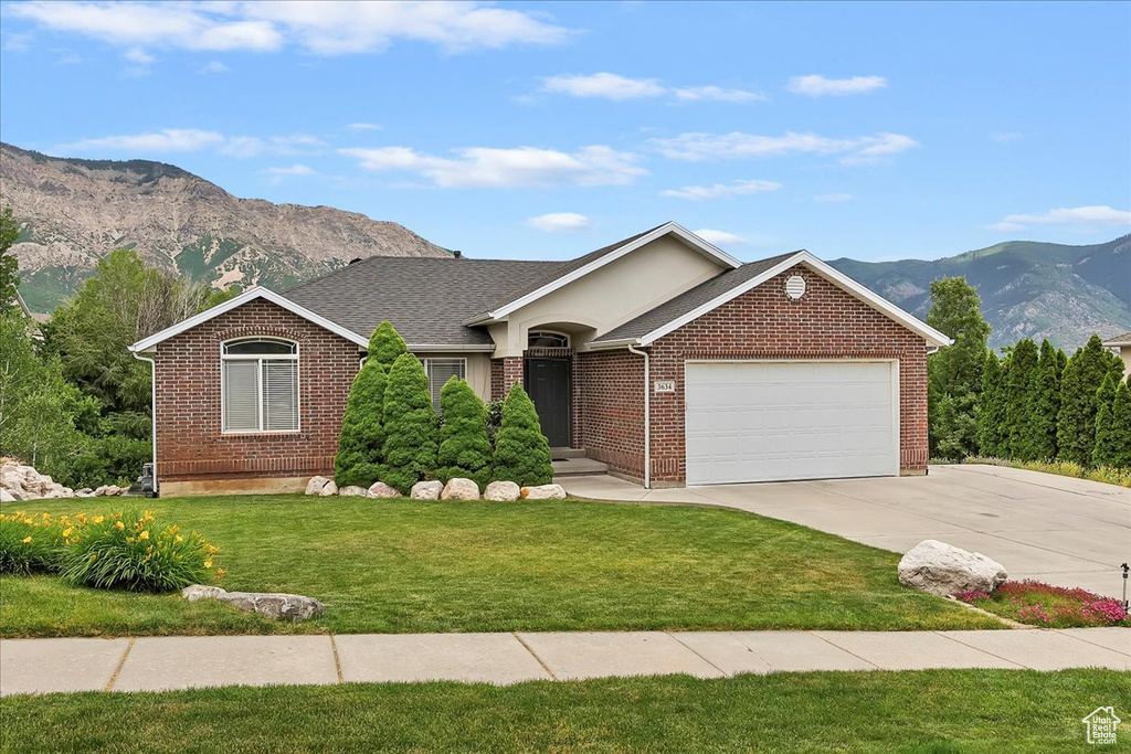 Ranch-style house featuring a mountain view, driveway, a garage, brick siding, and a front yard