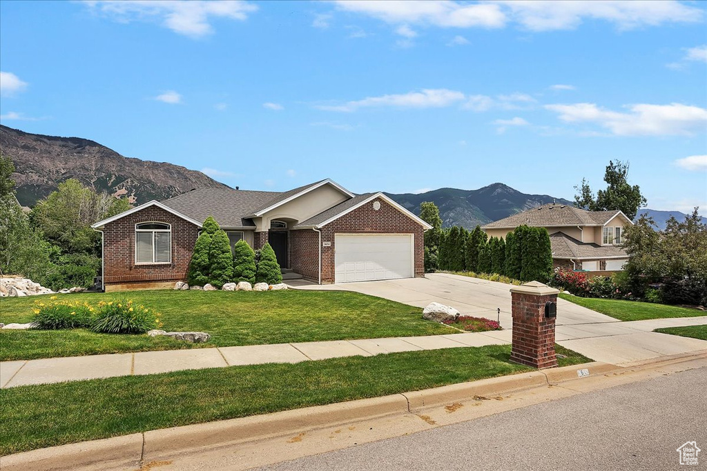 Ranch-style home with a mountain view, brick siding, driveway, an attached garage, and a front yard