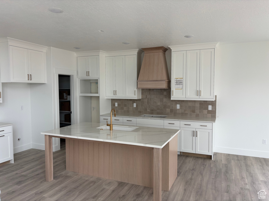 Kitchen featuring custom range hood, stovetop, light wood-style flooring, and a center island with sink