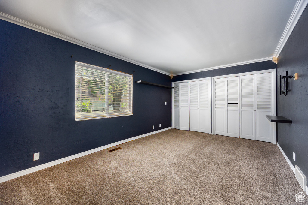 Unfurnished bedroom with crown molding, carpet flooring, and two closets