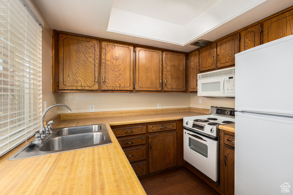 Kitchen featuring white appliances, brown cabinetry, and dark wood-type flooring