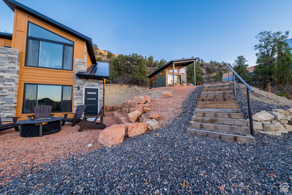 Back of house featuring a fire pit, stairs, stone siding, and a metal roof
