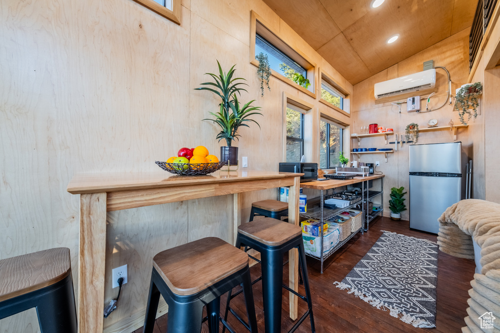Kitchen featuring freestanding refrigerator, a wall mounted AC, wood finished floors, high vaulted ceiling, and recessed lighting